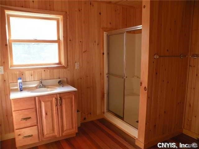 bathroom featuring walk in shower, wood walls, vanity, and wood-type flooring