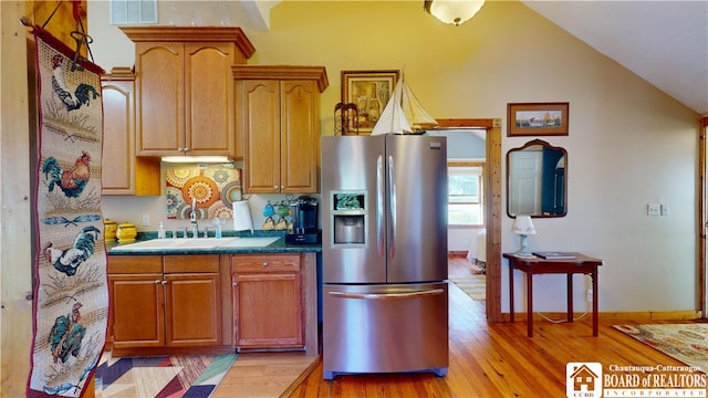 kitchen with sink, light hardwood / wood-style floors, stainless steel fridge, and vaulted ceiling