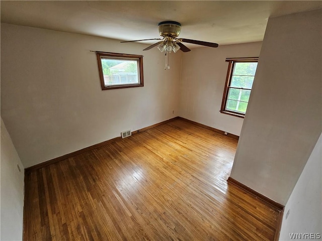 empty room with ceiling fan, a healthy amount of sunlight, and hardwood / wood-style flooring