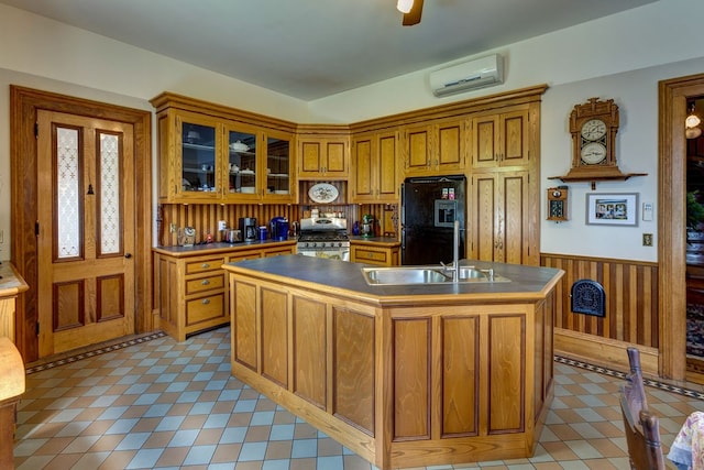 kitchen featuring a wall unit AC, black fridge, gas range, light tile floors, and a kitchen island with sink