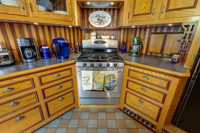 73 Elm St, Otsego, NY 13326 - kitchen with dark countertops, brown cabinetry, wood walls, and stainless steel gas range oven