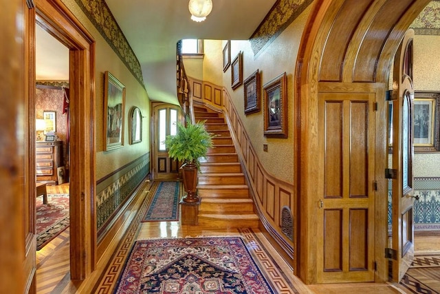 73 Elm St, Otsego, NY 13326 - hall featuring arched walkways, a wainscoted wall, stairs, and light wood-style flooring
