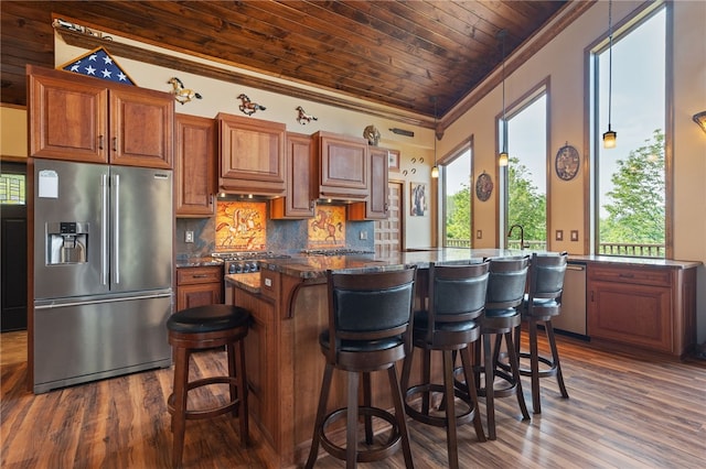 kitchen with a breakfast bar area, stainless steel appliances, dark stone countertops, kitchen peninsula, and brick ceiling