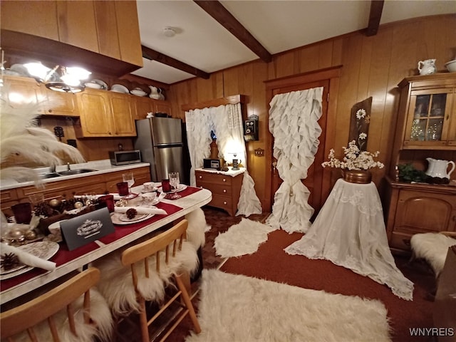 interior space featuring wood walls, stainless steel refrigerator, sink, and beam ceiling