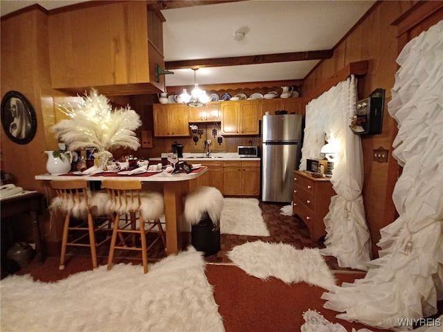 kitchen with beamed ceiling, wooden walls, stainless steel appliances, sink, and a breakfast bar area