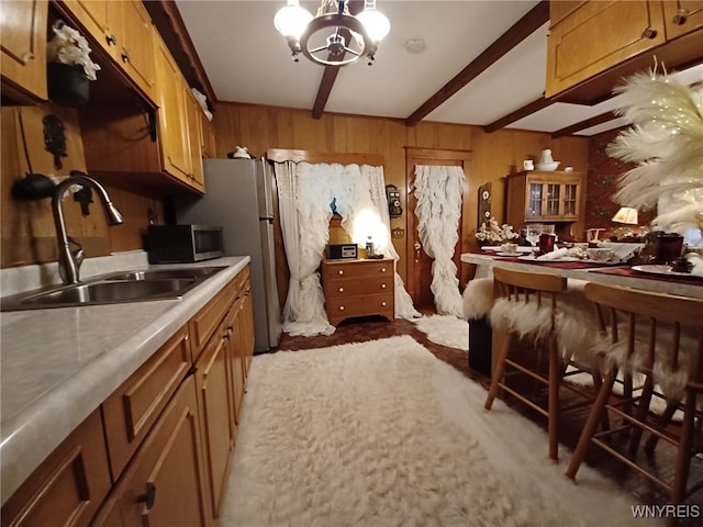 kitchen with sink, beamed ceiling, wooden walls, and a notable chandelier