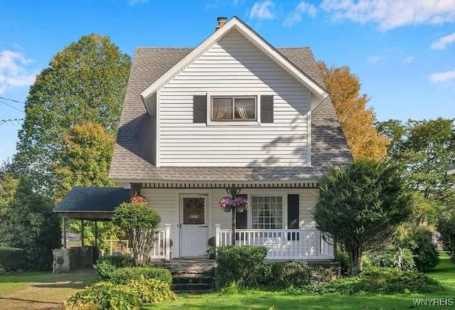 view of front of house with a shingled roof, covered porch, and a front lawn