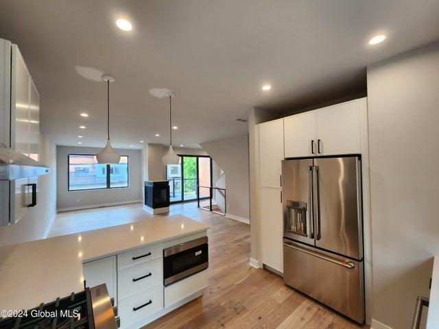 kitchen featuring light wood-type flooring, high quality fridge, built in microwave, decorative light fixtures, and white cabinets