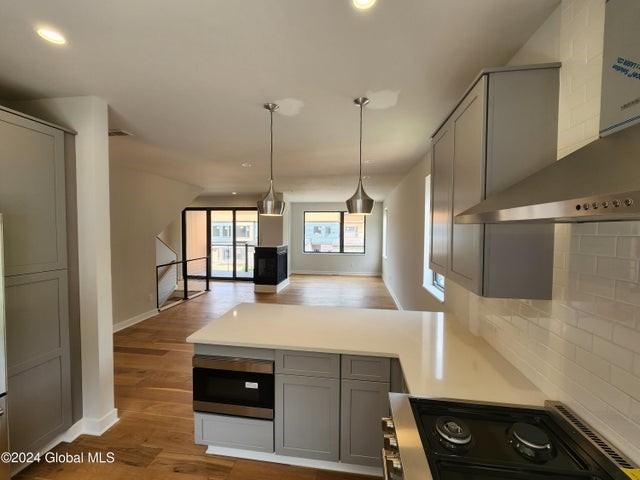 kitchen with wall chimney exhaust hood, dark hardwood / wood-style floors, stove, gray cabinets, and decorative backsplash