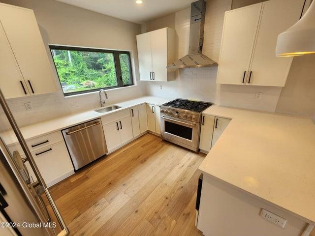 kitchen with appliances with stainless steel finishes, white cabinetry, wall chimney exhaust hood, and sink