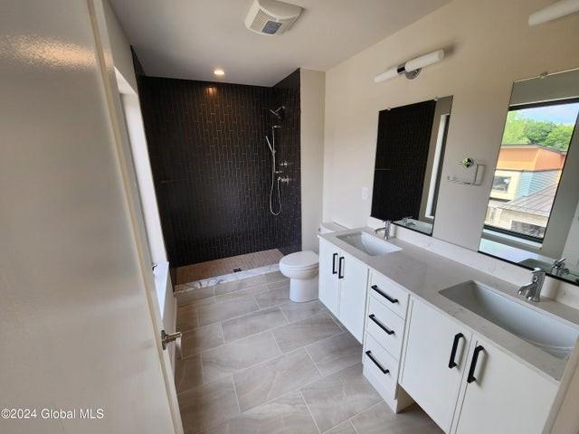 bathroom with tile patterned flooring, vanity, toilet, and tiled shower