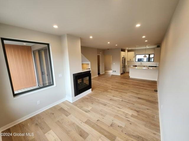 unfurnished living room featuring a multi sided fireplace and light hardwood / wood-style flooring