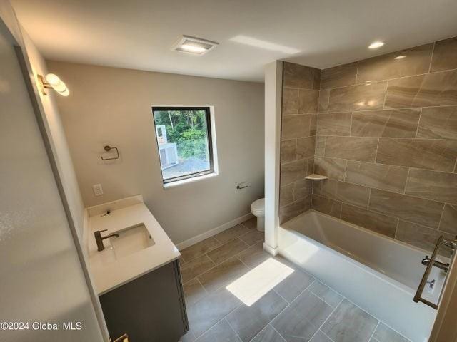 full bathroom with tiled shower / bath, tile patterned flooring, vanity, and toilet