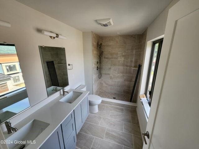 bathroom featuring a tile shower, tile patterned floors, vanity, and toilet