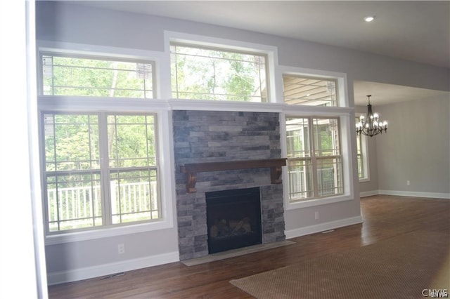 unfurnished living room with a fireplace, dark wood-type flooring, a chandelier, and plenty of natural light