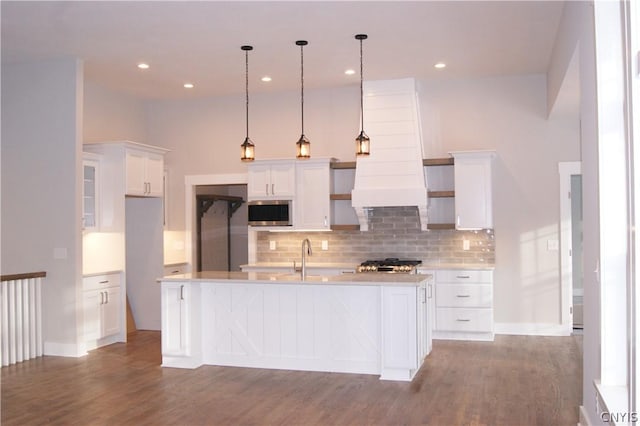 kitchen featuring hardwood / wood-style flooring, stainless steel microwave, pendant lighting, a kitchen island with sink, and white cabinets