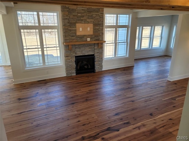 unfurnished living room with a fireplace, dark wood-type flooring, and a healthy amount of sunlight