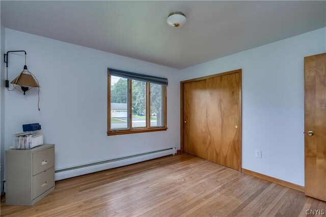 unfurnished bedroom with a closet, light wood-type flooring, and a baseboard heating unit