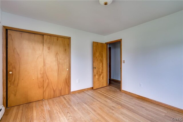 unfurnished bedroom with baseboard heating, a closet, and light hardwood / wood-style floors