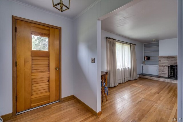 foyer entrance featuring light hardwood / wood-style flooring, a stone fireplace, a healthy amount of sunlight, and crown molding