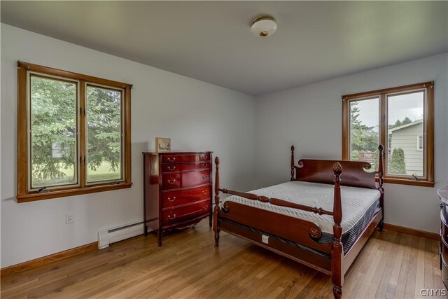 bedroom with light wood-type flooring, multiple windows, and a baseboard heating unit