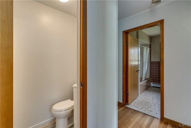 bathroom with shower / bathtub combination with curtain, a baseboard heating unit, hardwood / wood-style floors, toilet, and ornamental molding