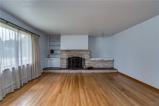 unfurnished living room featuring light wood-type flooring and a stone fireplace