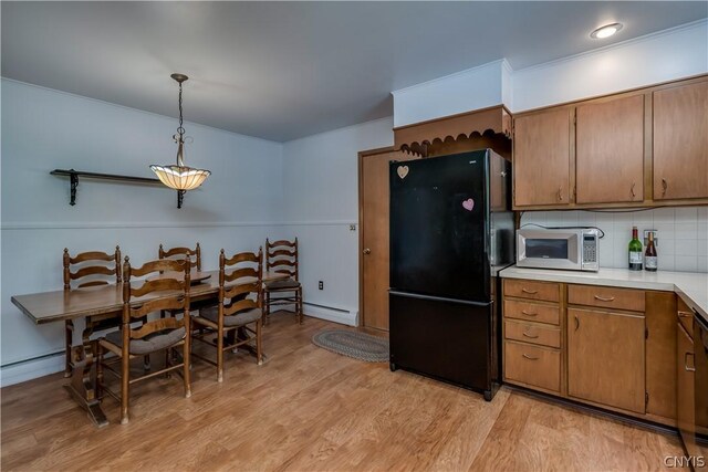 kitchen featuring hanging light fixtures, a baseboard radiator, decorative backsplash, black refrigerator, and light wood-type flooring