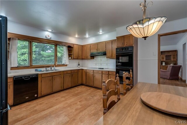 kitchen featuring black appliances, sink, hanging light fixtures, decorative backsplash, and light wood-type flooring