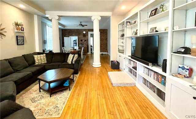 living room with decorative columns, ceiling fan, brick wall, and light hardwood / wood-style floors