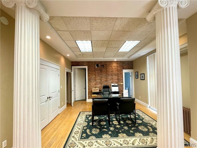 office featuring decorative columns, brick wall, light hardwood / wood-style flooring, and a paneled ceiling