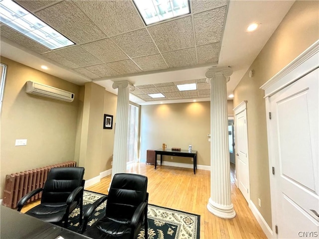 office space with a wall unit AC, ornate columns, radiator, hardwood / wood-style floors, and a drop ceiling