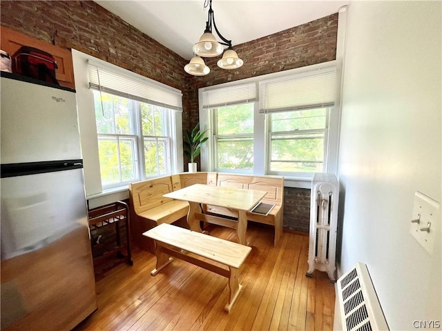 dining room featuring breakfast area, radiator heating unit, light hardwood / wood-style flooring, brick wall, and an inviting chandelier