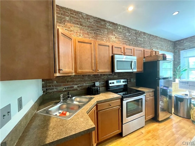 kitchen with sink, light wood-type flooring, brick wall, and appliances with stainless steel finishes