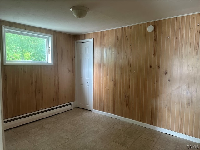 tiled empty room featuring wood walls and a baseboard radiator