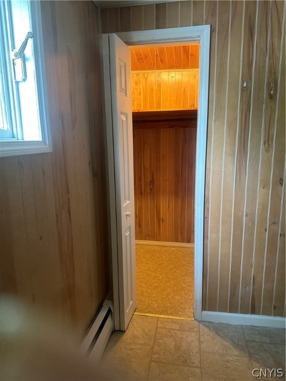 hall featuring wood walls, a baseboard heating unit, and tile floors