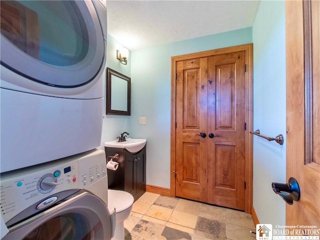 bathroom featuring stacked washer / dryer, vanity, and toilet