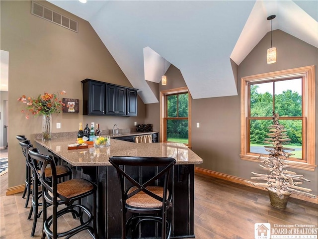 kitchen with light stone counters, light hardwood / wood-style flooring, kitchen peninsula, pendant lighting, and a breakfast bar