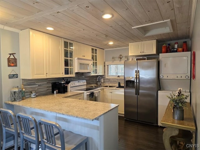 kitchen featuring kitchen peninsula, white cabinets, stacked washer and clothes dryer, and appliances with stainless steel finishes