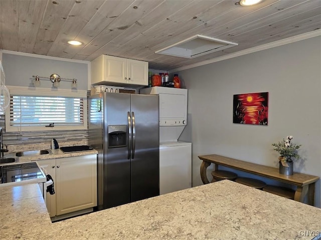 kitchen with white cabinetry, sink, stainless steel fridge with ice dispenser, stacked washer / drying machine, and wood ceiling