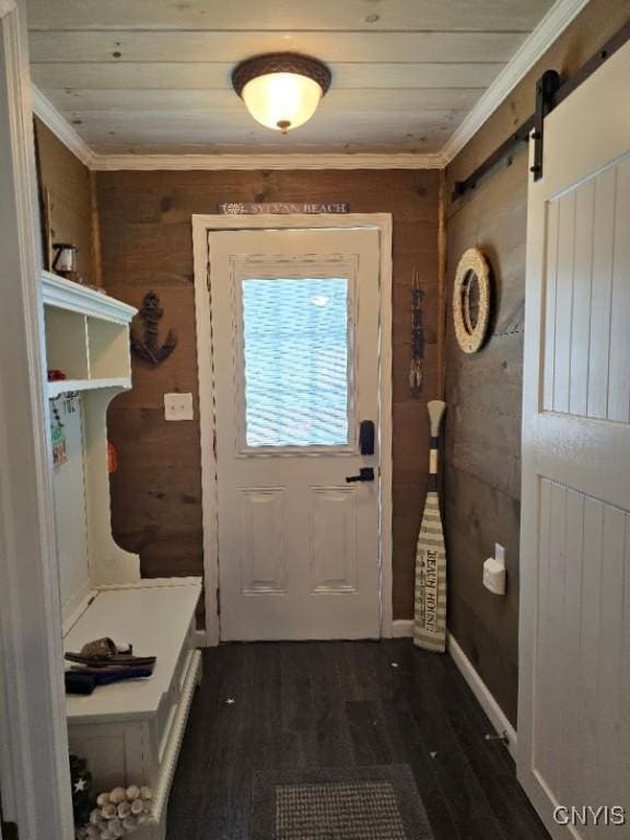 doorway to outside featuring ornamental molding, a barn door, dark hardwood / wood-style floors, and wooden walls