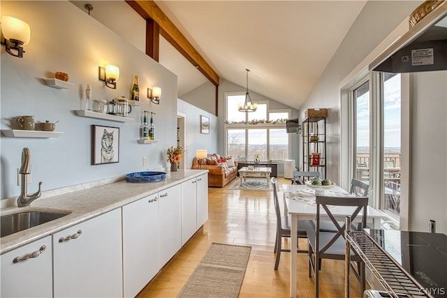 kitchen with light hardwood / wood-style floors, vaulted ceiling with beams, white cabinets, sink, and pendant lighting