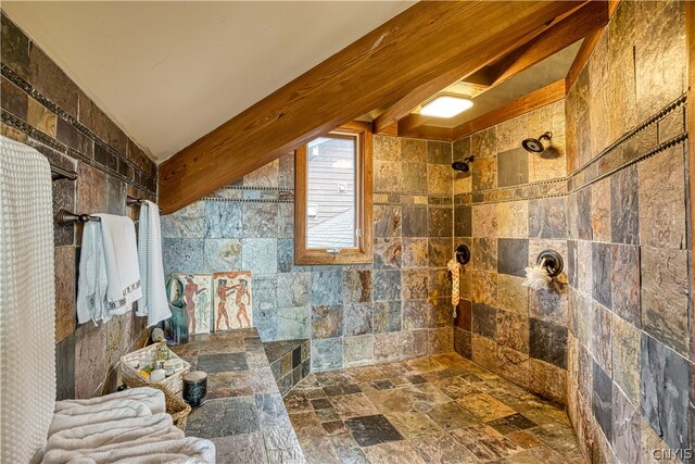 bathroom with a tile shower, beam ceiling, and tile walls