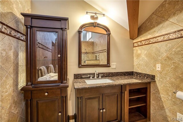 bathroom with vaulted ceiling with beams, oversized vanity, and tile walls