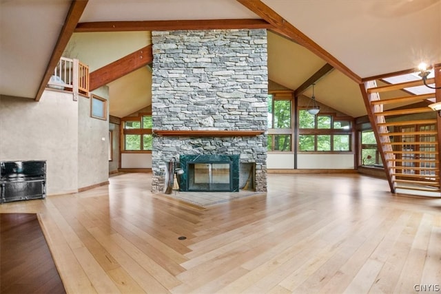 unfurnished living room featuring an inviting chandelier, light hardwood / wood-style flooring, a stone fireplace, high vaulted ceiling, and beamed ceiling