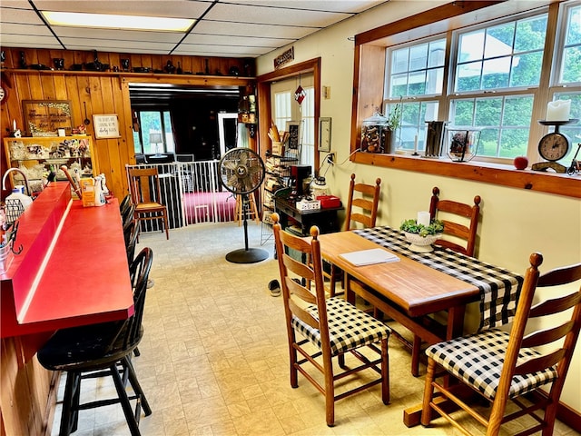 dining area with a drop ceiling, wooden walls, and plenty of natural light