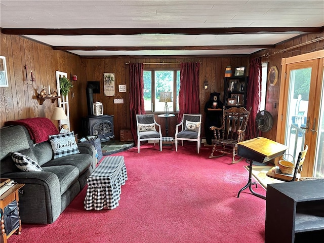 living room featuring carpet floors, beamed ceiling, wood walls, and a wood stove