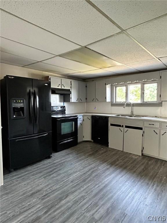 kitchen with a paneled ceiling, white cabinetry, black appliances, wood-type flooring, and sink