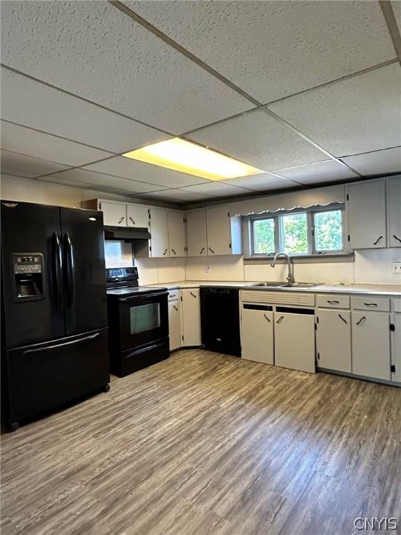 kitchen featuring under cabinet range hood, a sink, light wood-style floors, light countertops, and black appliances