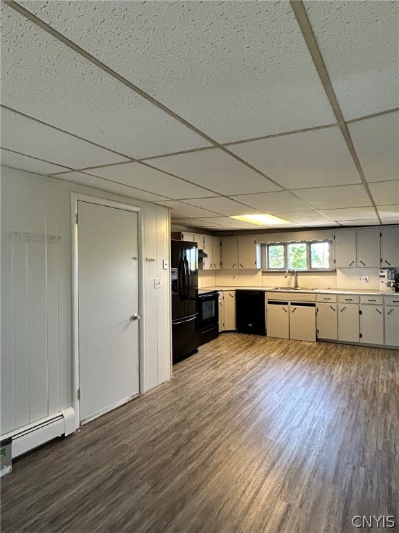 kitchen with a paneled ceiling, hardwood / wood-style flooring, black appliances, baseboard heating, and sink